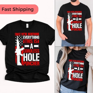 Könnte beinhalten: Schwarze T-Shirts mit einem rot-weißen Grafikdesign. Das Design enthält den Text "SINCE WE'RE REDEFINING EVERYTHING THIS IS A CORDLESS HOLE PUNCHER" und eine Gewehrillustration. Die T-Shirts werden vor weißem Hintergrund präsentiert.