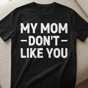Könnte beinhalten: Schwarzes T-Shirt mit dem weißen Text "MY MOM - DON'T - LIKE YOU". Der Text ist zentriert und in fetter, serifenloser Schrift. Das T-Shirt besteht aus weichem Material und hat kurze Ärmel.