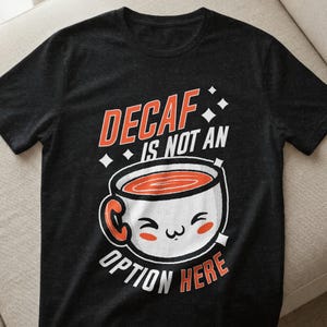 Könnte beinhalten: Schwarzes T-Shirt mit dem Text "DECAF IS NOT AN OPTION HERE" in Orange und Weiß. Die Grafik zeigt eine lächelnde Kaffeetasse mit orangefarbenem Kaffee. Das Shirt besteht aus einem weichen Material.