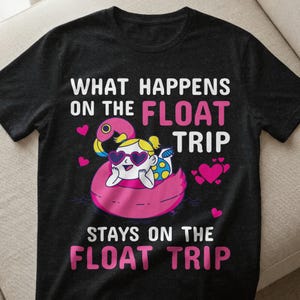 Könnte beinhalten: Schwarzes T-Shirt mit dem Text "WHAT HAPPENS ON THE FLOAT TRIP STAYS ON THE FLOAT TRIP". Das Shirt zeigt einen Cartoon einer Person auf einem rosa Flamingo-Schwimmer mit herzförmigen Sonnenbrillen. Rosa Herzen sind um das Design verstreut.