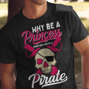 Könnte beinhalten: Dunkelgraues T-Shirt mit Piratenmotiv. Das Design zeigt einen Totenkopf mit Augenklappe und gekreuzten rosa Piratenhüten sowie den Text "WHY BE A Princess WHEN YOU CAN BE A Pirate."