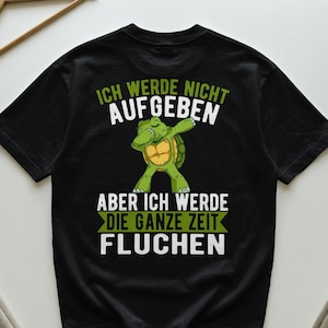 Könnte beinhalten: Schwarzes T-Shirt mit einer grünen Schildkröten-Grafik, die dabbt. Der Text auf dem Shirt lautet "ICH WERDE NICHT AUFGEBEN, ABER ICH WERDE DIE GANZE ZEIT FLUCHEN" in Weiß und Grün.
