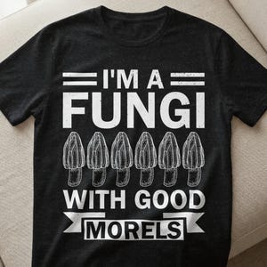 Könnte beinhalten: Schwarzes T-Shirt mit weißem Text und Illustrationen. Der Text lautet "I'M A FUNGI WITH GOOD MORELS". Darunter befinden sich sechs detaillierte Zeichnungen von Morchelpilzen. Das Shirt besteht aus einem weichen, dunklen Stoff.