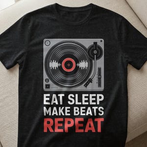 May include: Black t-shirt featuring a turntable graphic with a vinyl record. The design includes the text "EAT SLEEP MAKE BEATS REPEAT" in white and red. The shirt is made of a soft material.