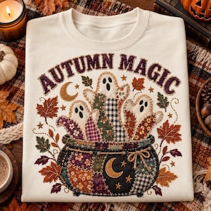 Op de afbeelding: Een crèmekleurig sweatshirt met ronde hals en een grafische print van een patchwork ketel gevuld met drie geesten. De tekst "AUTUMN MAGIC" staat in een boog boven de ketel, omringd door herfstbladeren, sterren en een maansikkel.