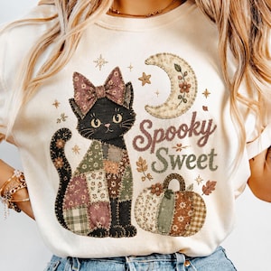 May include: A cream-colored t-shirt featuring a graphic of a black cat with a patchwork body and a bow on its head. Beside the cat is a crescent moon and a patchwork pumpkin. The text "Spooky Sweet" is printed in brown script next to the cat.