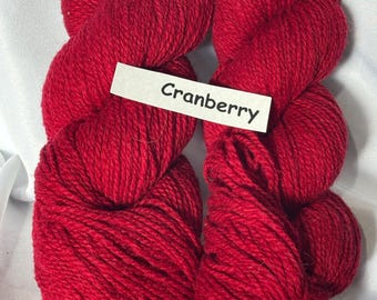 May include: Four skeins of vibrant red yarn, labeled "Cranberry". The yarn is tightly wound, showing a textured surface. The color is a deep, rich red, perfect for knitting or crocheting projects. The yarn is displayed against a white background.