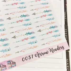 Puede incluir: Una hoja de pegatinas con ilustraciones de acuarela de flechas con plumas y corazones. Las pegatinas están etiquetadas como "0037 Arrow Headers".