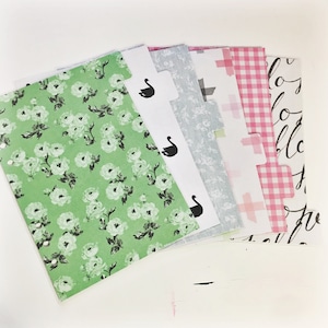 May include: A set of six colorful patterned dividers for a planner or notebook. The dividers feature a floral pattern, a gray and white pattern, a pink and white gingham pattern, a black and white pattern, and a black and white swan pattern.