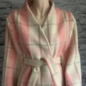 Puede incluir: Una chaqueta cruzada de manga larga con un patr&oacute;n de cuadros en rosa, crema y gris. La prenda tiene un cuello ancho, un cintur&oacute;n de lazo a juego en la cintura y detalles visibles de puntada de fest&oacute;n blanca en el dobladillo y los pu&ntilde;os.