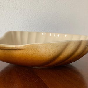 May include: A large, white ceramic bowl with a brown glaze. The bowl is shaped like a seashell and has a wavy, organic design.