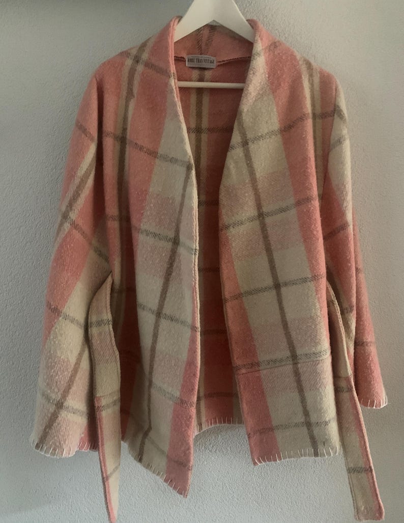 Puede incluir: Una chaqueta de manga larga abierta por delante con un patr&oacute;n de cuadros en rosa, crema y beige. La prenda tiene un cuello ancho, un cintur&oacute;n para anudar a la cintura y costuras visibles a lo largo del dobladillo. Una etiqueta est&aacute; cosida.