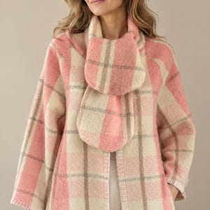 Puede incluir: Un cárdigan abierto de manga larga, suave y difuso, con un patrón de cuadros grandes en tonos rosa empolvado, crema y marrón claro. La prenda incluye una bufanda a juego drapeada alrededor del cuello y tiene detalles de costura blanca.