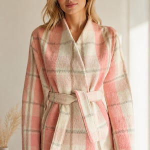 Puede incluir: Una chaqueta de manga larga abierta por delante con un patr&oacute;n de cuadros en rosa, crema y gris. La prenda incluye un cintur&oacute;n de tela a juego en la cintura, un cuello ancho y detalles de costura visible en el dobladillo y los pu&ntilde;os.