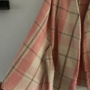 Puede incluir: Una capa suave de frente abierto con un patr&oacute;n de cuadros en tonos rosa claro, crema y beige. La prenda tiene una silueta amplia y fluida con detalles de puntada de fest&oacute;n visibles a lo largo del dobladillo inferior y un cuello sin solapas.