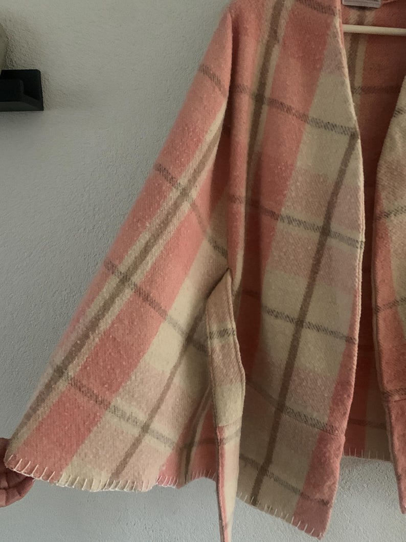 Puede incluir: Una capa suave de frente abierto con un patr&oacute;n de cuadros en tonos rosa claro, crema y beige. La prenda tiene una silueta amplia y fluida con detalles de puntada de fest&oacute;n visibles a lo largo del dobladillo inferior y un cuello sin solapas.