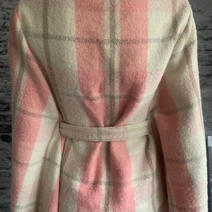 Puede incluir: Una chaqueta de manga larga con un patr&oacute;n de cuadros en tonos rosa suave, crema y gris claro. La prenda incluye un cintur&oacute;n de tela a juego en la cintura, un cuello ancho y costuras visibles a lo largo del dobladillo inferior texturizado.