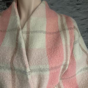 Puede incluir: Un abrigo de manga larga con un patr&oacute;n de cuadros grandes en tonos rosa suave, crema y marr&oacute;n claro. La prenda presenta un cuello chal ancho, un dise&ntilde;o cruzado y un cintur&oacute;n de tela a juego en la cintura con un acabado texturizado.