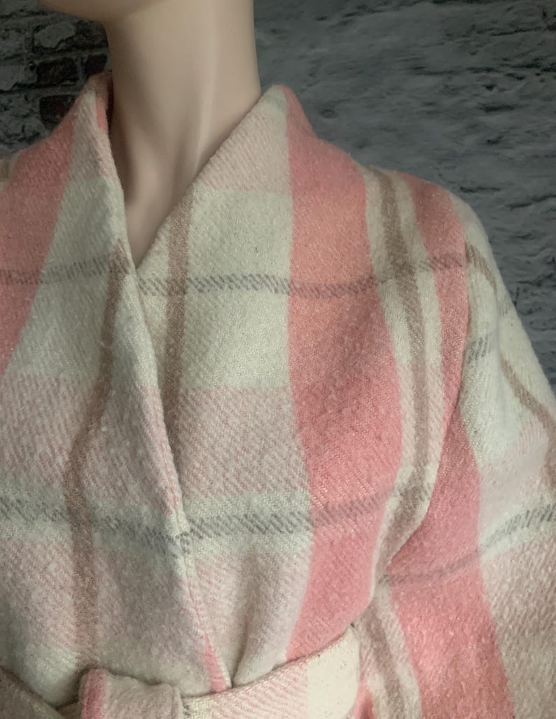 Puede incluir: Un abrigo de manga larga con un patr&oacute;n de cuadros grandes en tonos rosa suave, crema y marr&oacute;n claro. La prenda presenta un cuello chal ancho, un dise&ntilde;o cruzado y un cintur&oacute;n de tela a juego en la cintura con un acabado texturizado.