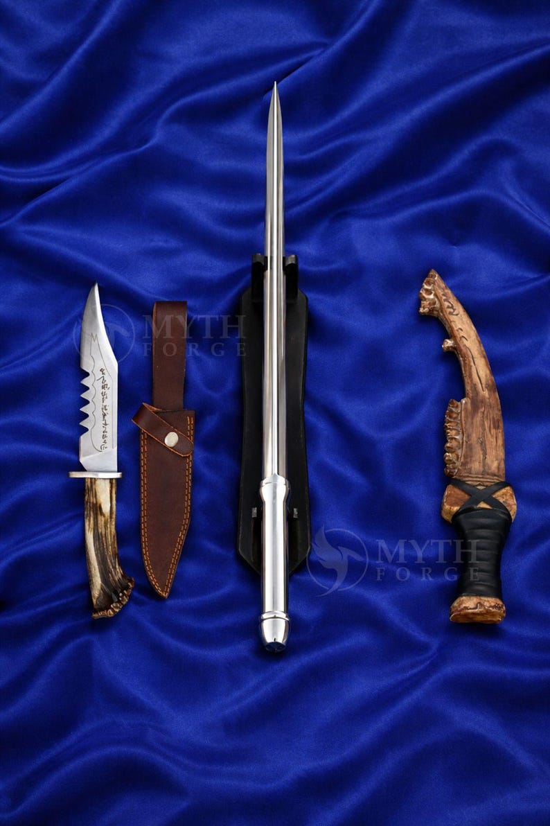 May include: An assortment of blades and knives are displayed on a blue satin surface. The collection includes a long, slender silver blade in a black stand, a knife with a serrated edge and antler handle, and a curved knife with a wooden handle.