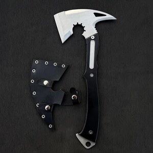 May include: A tactical axe with a silver blade and a black handle, shown with a black leather sheath. The axe head has a unique design with a curved edge and a gear-like cutout. The handle is black with silver accents.