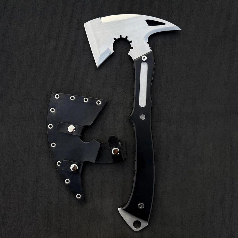 May include: A tactical axe with a silver blade and a black handle, shown with a black leather sheath. The axe head has a unique design with a curved edge and a gear-like cutout. The handle is black with silver accents.