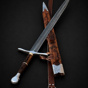 May include: A double-edged sword with a patterned Damascus steel blade, a wooden handle with silver accents, and a rounded silver pommel. It is accompanied by a matching wooden scabbard with silver fittings and a brown leather belt with a metal buckle.