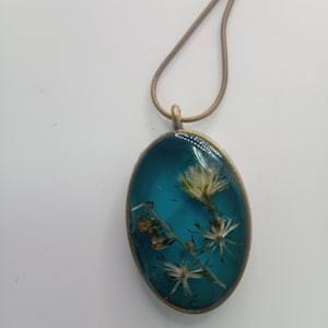 Collar con bisel de tono oro envejecido. Con fondo de color esmeralda y flores silvestres secas y preservadas.