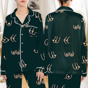 May include: Dark green pajama set with a repeating pattern of stylized breasts in a light peach color. The set includes a button-down top with white piping and matching pants. The pajamas are made of a silky material.