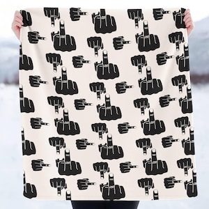 May include: A cream-colored blanket featuring a repeating pattern of black hand gestures, each displaying the middle finger. The design is bold and graphic, creating a striking visual impact. The blanket is held up against a snowy background.