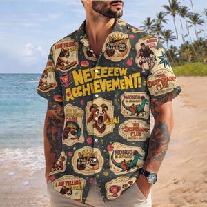 May include: Dark gray button-down shirt with a collage of cartoon images and text. The shirt features phrases like "NEW ACHIEVEMENT!" and "I AM YELLING CARL!" The design includes cats, dinosaurs, and other whimsical elements.