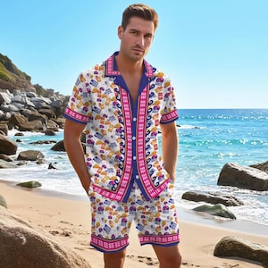 May include: A matching white button-down shirt and shorts set with a repeating pattern of tacos, burritos, and other food items. The shirt and shorts have blue and pink trim. The outfit is worn on a beach.