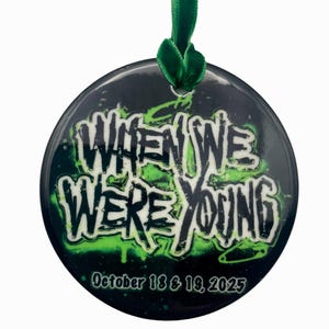 May include: A round ornament with the text "WHEN WE WERE YOUNG" in white and green, set against a black background with green accents. The ornament includes the date "October 18 & 19, 2025" and is suspended by a green ribbon.