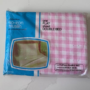 May include: A packaged double bed flat sheet in a pink and white gingham pattern. The packaging is blue and white with text that reads "no-iron muslin" and "one flat sheet double bed". The finished size is 206 cm by 251 cm.