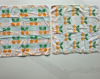 Pode incluir: Dois panos de cozinha vintage com um padrão repetido de frutas laranja e folhas verdes. Os panos têm um fundo azul claro com listras laranja e brancas. Os panos são feitos de um material macio e absorvente.