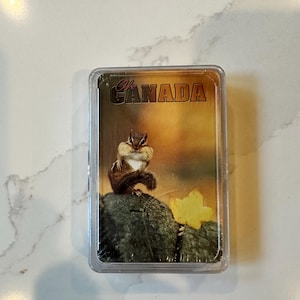 May include: A clear plastic case featuring a chipmunk on a rock with a yellow leaf. The background is a blurred landscape. The text "CANADA" is printed on the case.