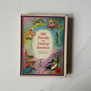 May include: A vintage hardcover book titled "Old Friends and Lasting Favorites." The cover features colorful illustrations of whimsical characters, including a cat, a witch, and a genie. The book has a purple border and is set against a white marble surface.