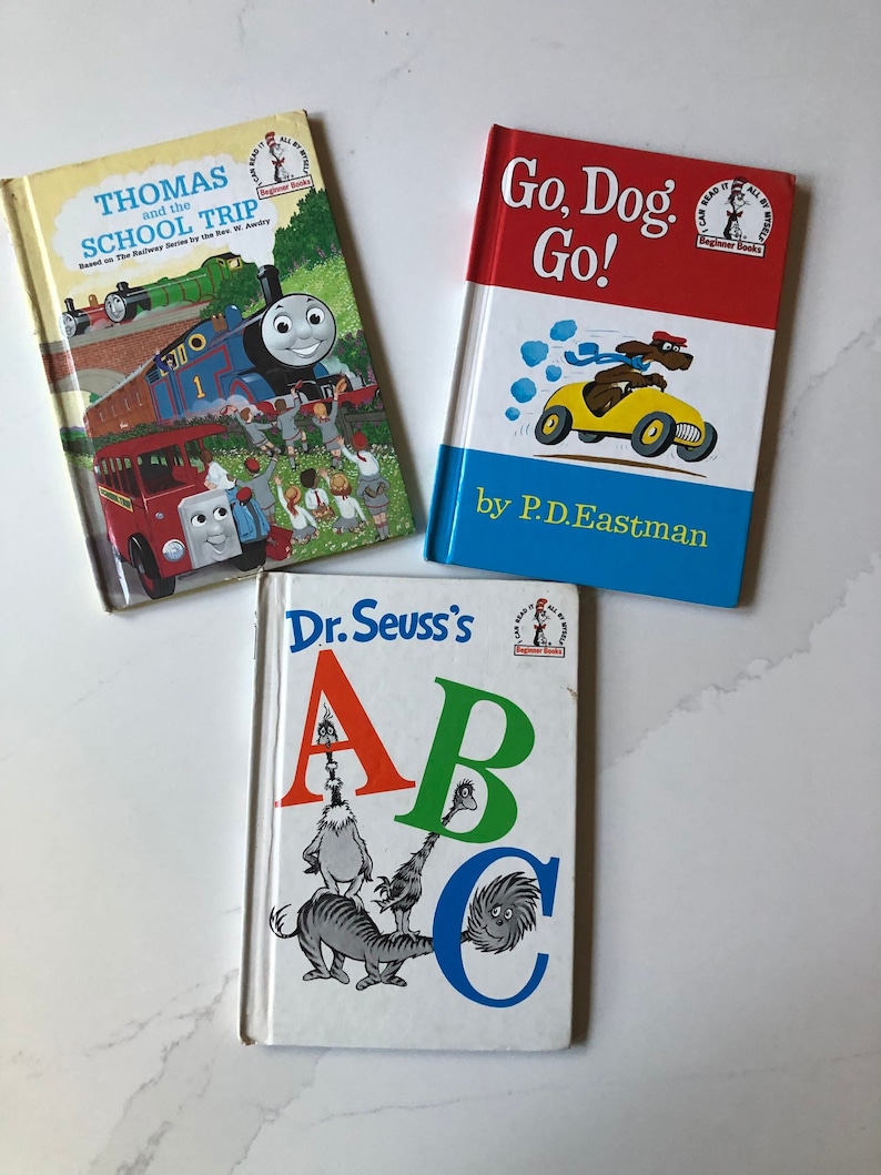 May include: Three children's books are displayed. The top left book is titled "Thomas and the School Trip" with an illustration of a train. The top right book is "Go, Dog. Go!" with a dog driving a yellow car. The bottom book is "Dr. Seuss's ABC".