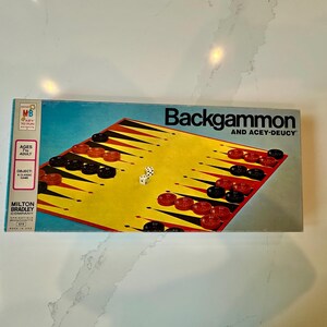 May include: Vintage Milton Bradley Backgammon game box. The box features a yellow and black game board with red and black game pieces. The dice are white. The box reads "Backgammon and Acey-Deucy".