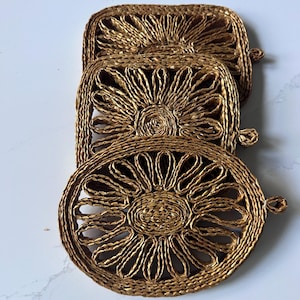 May include: Three woven golden-brown coasters in different shapes: square, rectangular, and oval. Each coaster features a sunburst design in the center and a small loop for hanging. These decorative coasters are ideal for protecting surfaces from heat and moisture.