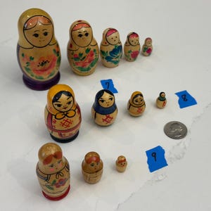 May include: A collection of wooden nesting dolls, also known as Matryoshka dolls, in various sizes. The dolls are painted with floral and geometric designs, featuring colors like red, yellow, blue, and green. The largest doll is approximately 6 inches tall.