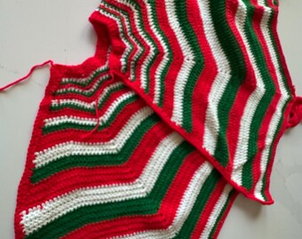May include: Two handmade crochet Christmas tree skirts. The skirts feature a zig-zag pattern in red, white, and green. Each skirt has a tassel at the end of the points. The skirts are made of a soft, textured yarn.