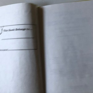 May include: Open book with a page featuring the text "This Book Belongs To..." and lines for writing. A black and white illustration of a figure holding a banner is on the left side of the page. The book's edge has a yellow and green pattern.