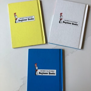 May include: Three Beginner Books with colorful covers. The books are yellow, white, and blue. Each book features the text "I CAN READ IT ALL BY MYSELF Beginner Books" and an illustration of a character in a red and white striped hat.