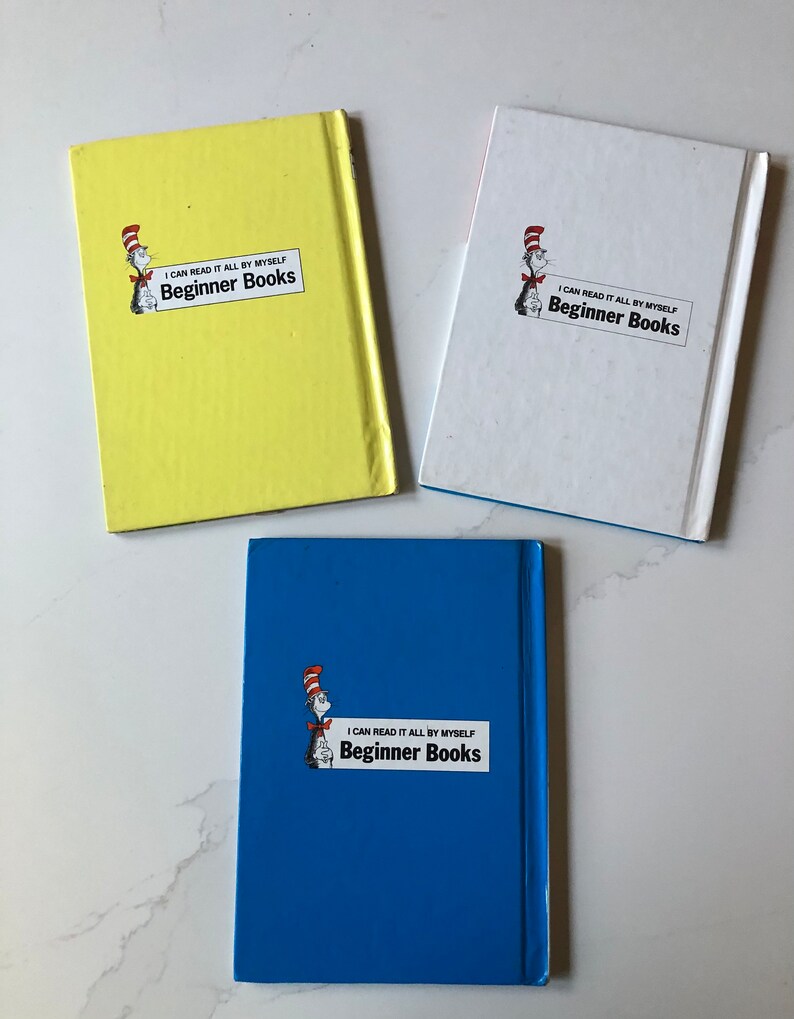 May include: Three Beginner Books with colorful covers. The books are yellow, white, and blue. Each book features the text "I CAN READ IT ALL BY MYSELF Beginner Books" and an illustration of a character in a red and white striped hat.