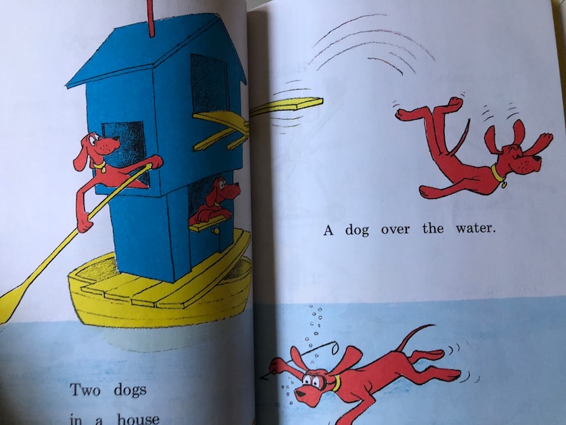 May include: A children's book illustration shows red dogs in various scenes. One dog rows a boat with a blue house, while another jumps over water. The text reads, "Two dogs in a house" and "A dog over the water."