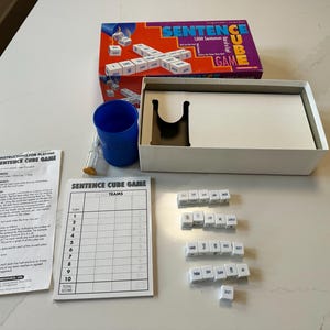 May include: A Sentence Cube Game set, featuring a box with the game title and a box of white cubes with words. Includes a blue cup, timer, score sheet, and instructions. The game is designed for multiple players.