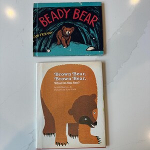 May include: Two children's books. The top book is titled Beady Bear by Don Freeman, featuring a brown bear in a dark cave. The bottom book is titled Brown Bear, Brown Bear, What Do You See? by Bill Martin, Jr. with pictures by Eric Carle, showing a large brown bear illustration.