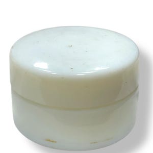 May include: A small, round, off-white jar with a matching lid. The jar appears to be made of a smooth, opaque material. The lid sits snugly on top of the jar, creating a seamless appearance. The jar is likely used for storing creams or other small items.