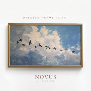 May include: A rectangular landscape painting in a gold frame depicting a flock of birds flying in a diagonal formation across a sky filled with white and blue clouds. The text PREMIUM FRAME TV ART and NOVUS VINTAGE ART appear above and below.